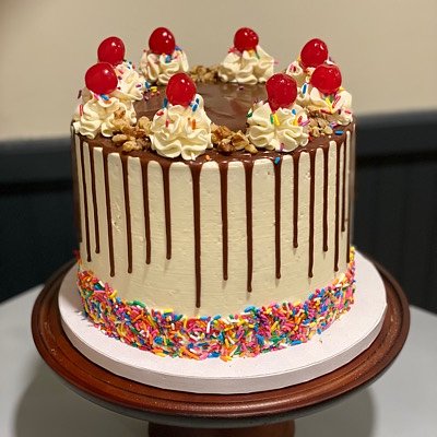 Signature Item- Banana Split Cake  Chocolate, Vanilla, Strawberry Cake Layers. Layered With Strawberry Preserves, Banana Cream Custard And Fresh Banana. Topped With Vanilla Buttercream, Chocolate Ganache Drip, Maraschino Cherries, Crushed Walnuts And Sprinkles (Available In 6”or 8”)